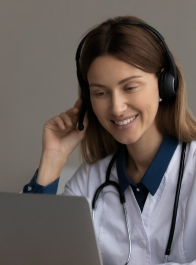 Happy friendly female doctor in headset using laptop